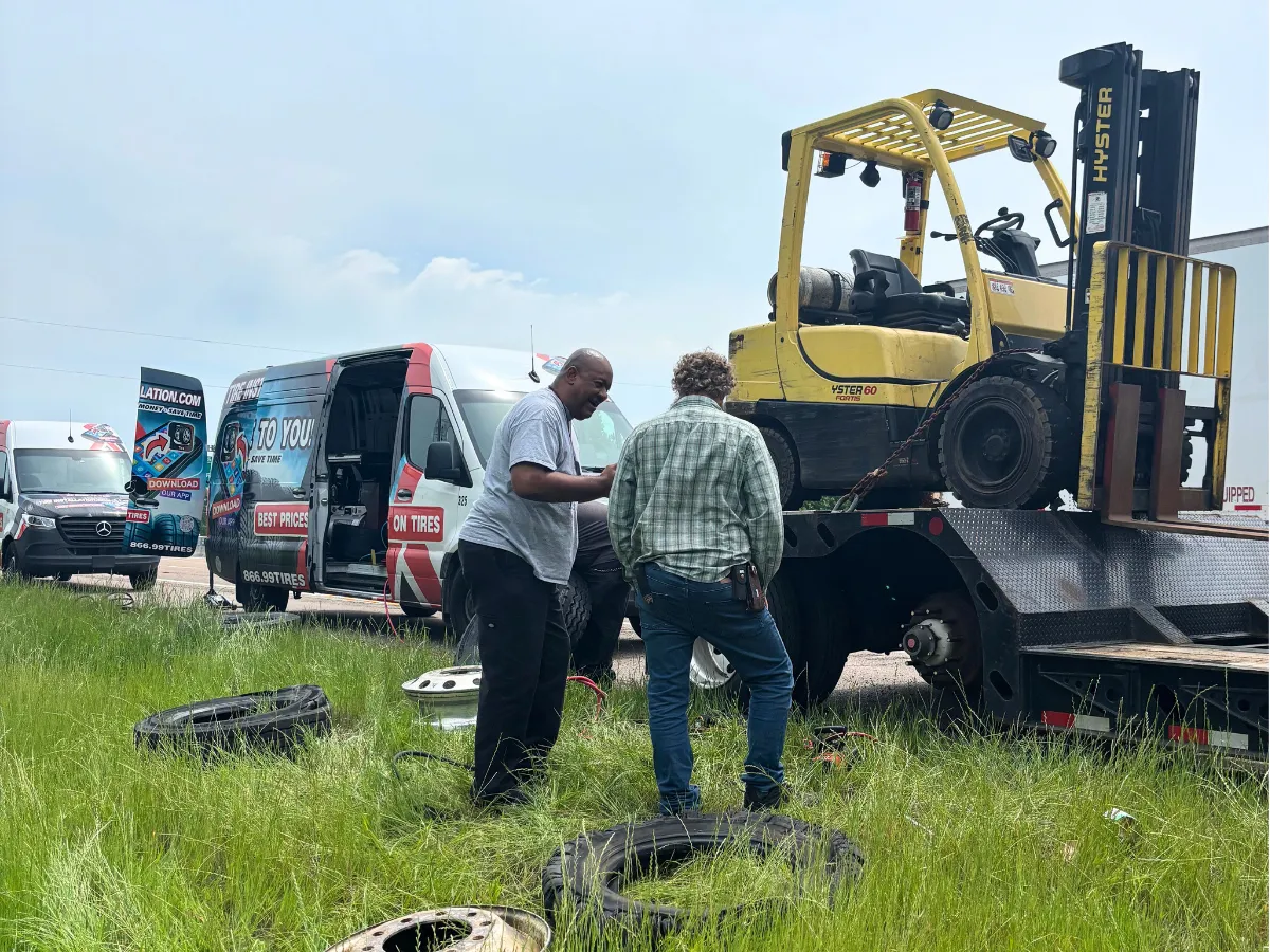 Mobile tire technician talking with a truck driver beside the service vans while replacing a commercial tire on site