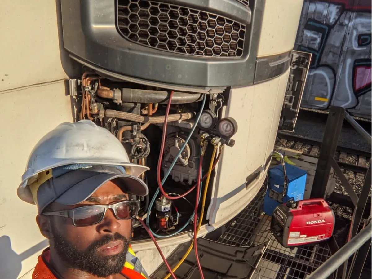 Technician in a hard hat with refrigerant gauges hooked to a trailer reefer unit during an on-site repair
