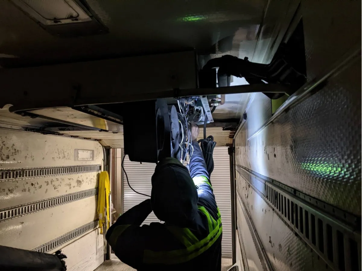 Technician inside a reefer trailer working overhead on the ceiling evaporator and fan assembly