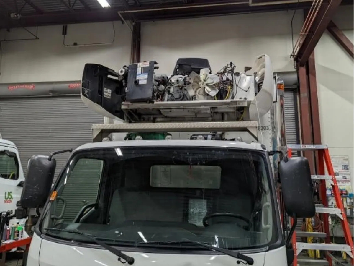 Reefer unit on top of a box truck cab opened up for repair with the fan and compressor exposed