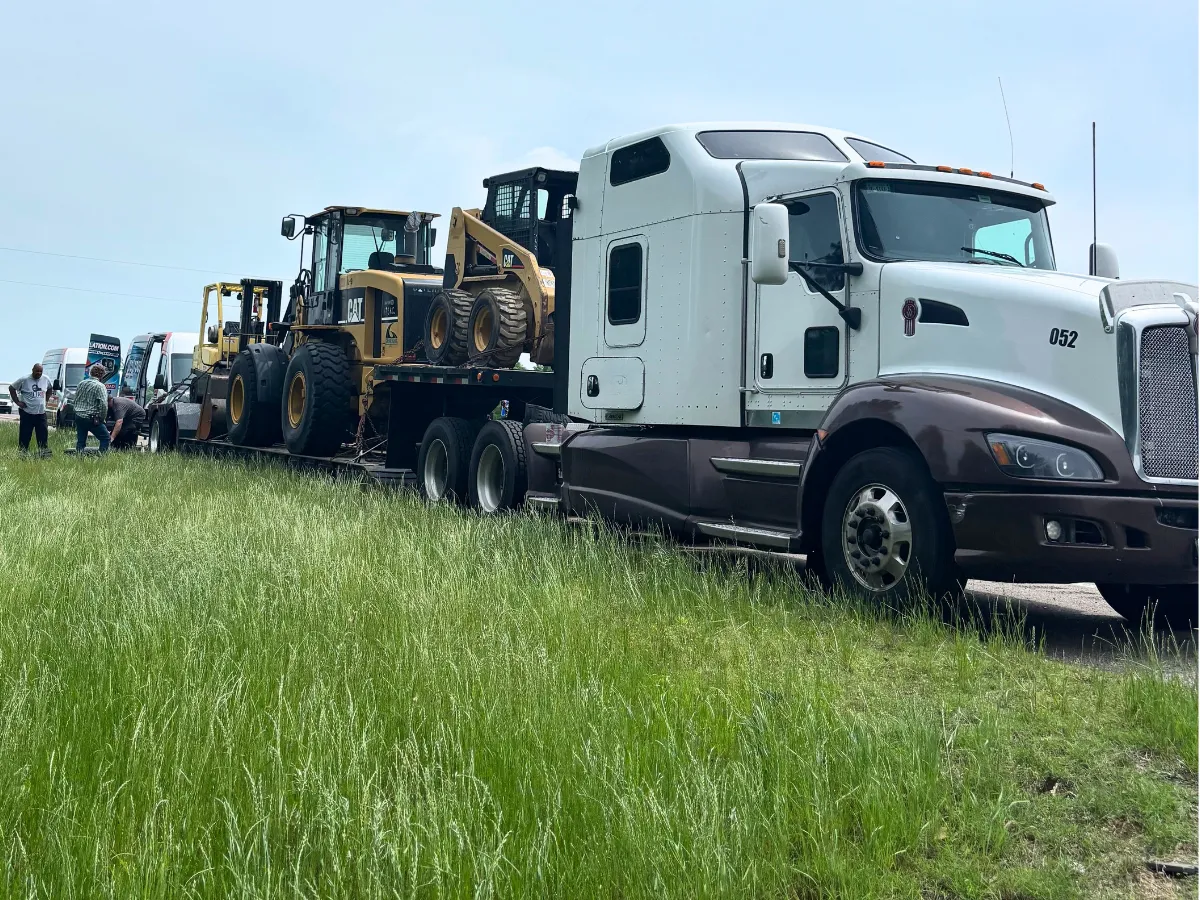 Semi truck hauling a CAT wheel loader on a lowboy getting a roadside tire change