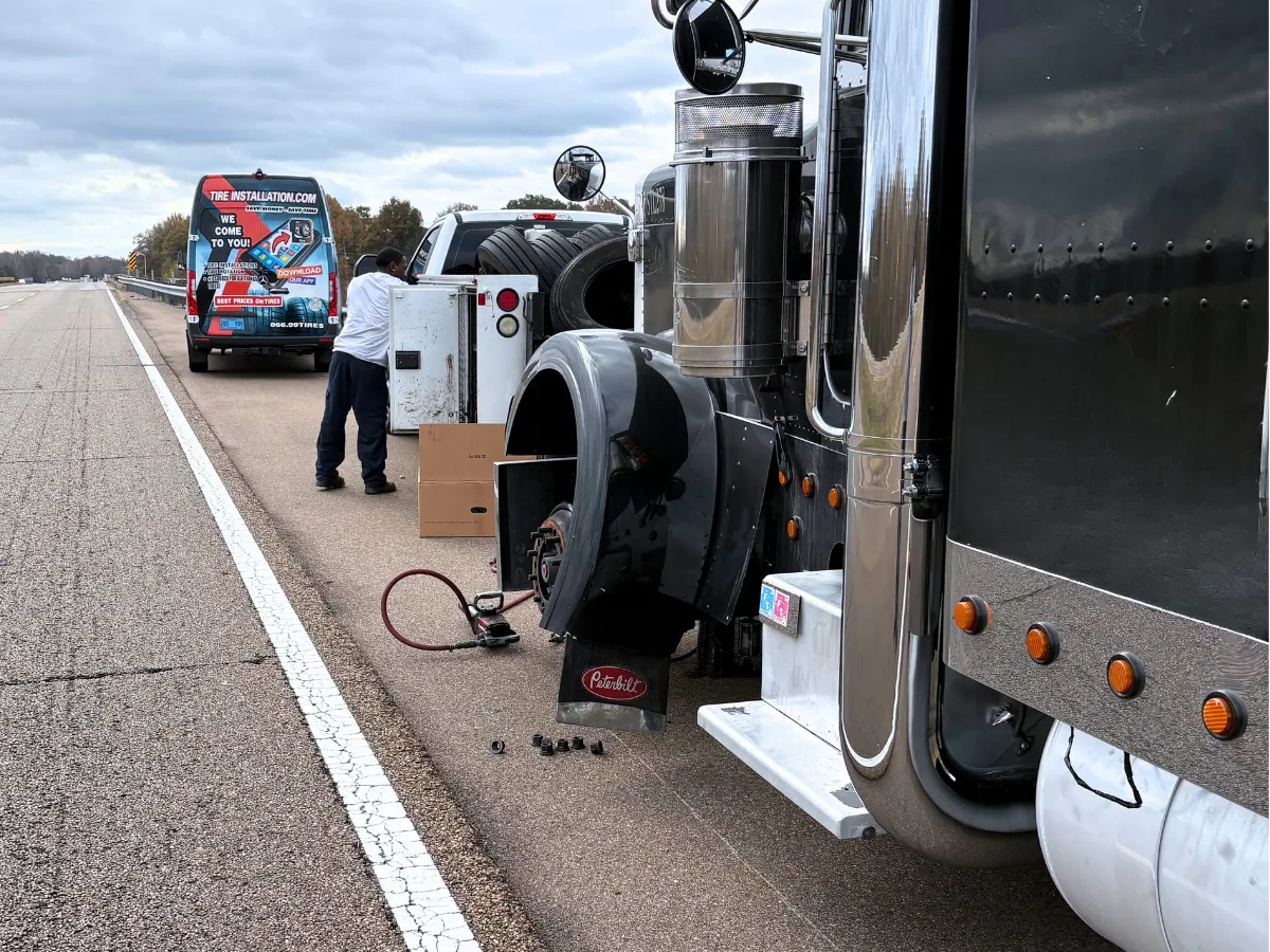 Mobile technician changing a steer tire on a semi truck on the roadside, with the tire installation service van parked behind