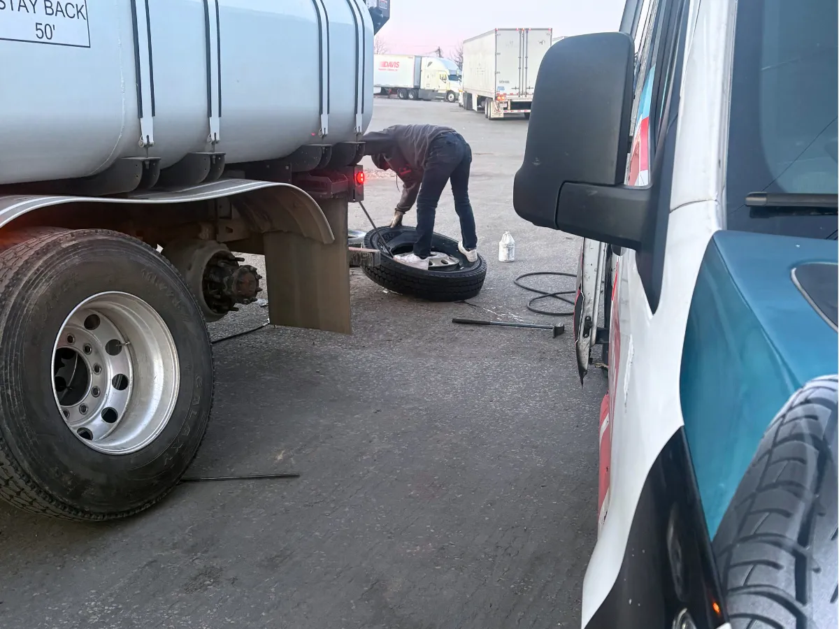 Technician changing a tire on a water truck at a lot with the mobile tire van alongside